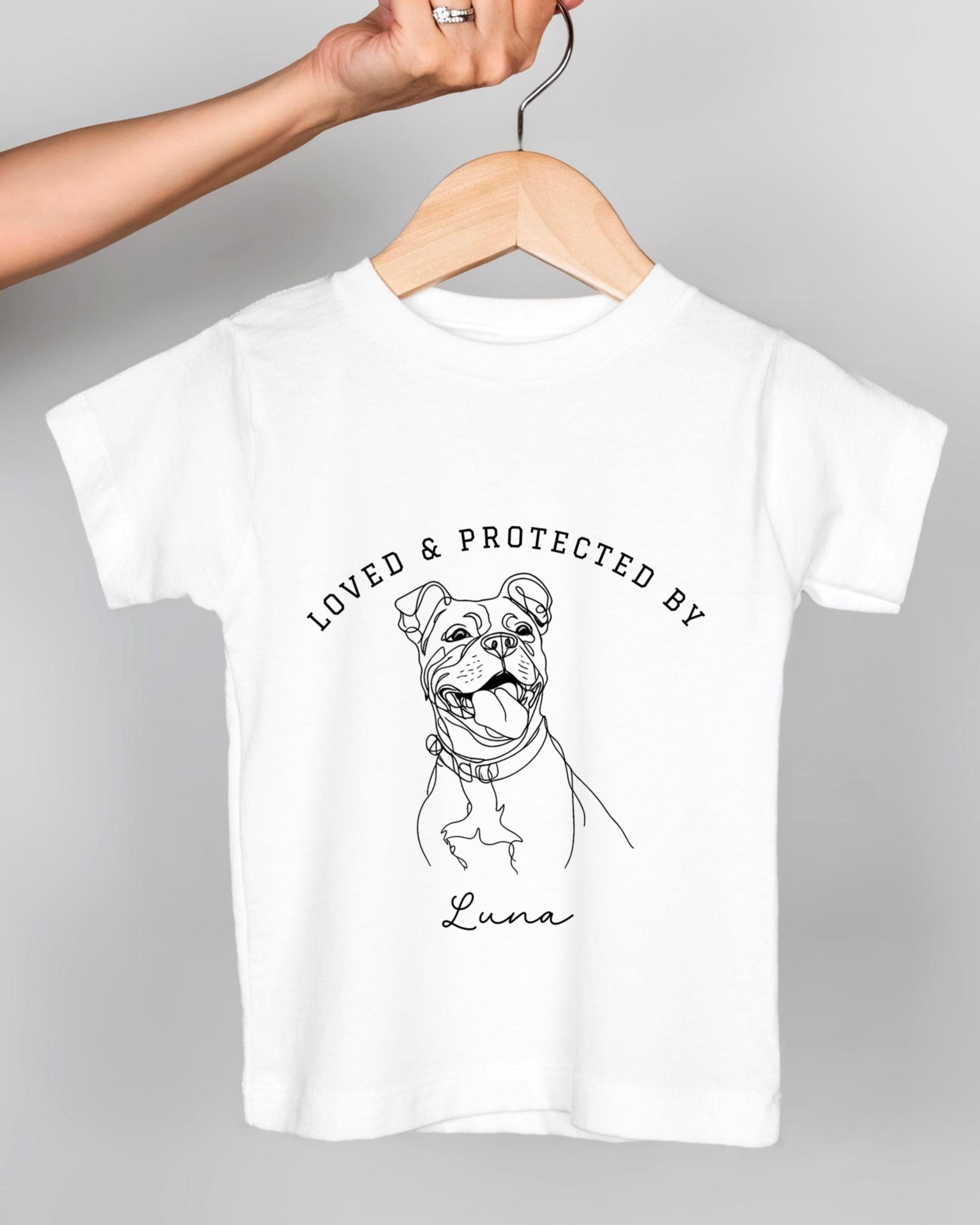 A white t-shirt with a black and white illustration of a dog and the text "LOVED & PROTECTED BY Luna" printed on it.
