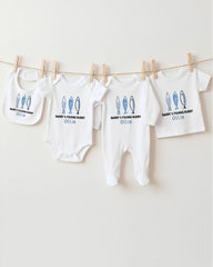 A row of four white baby clothes with blue fish designs, each with a personalized name printed on it, hanging on a clothesline.