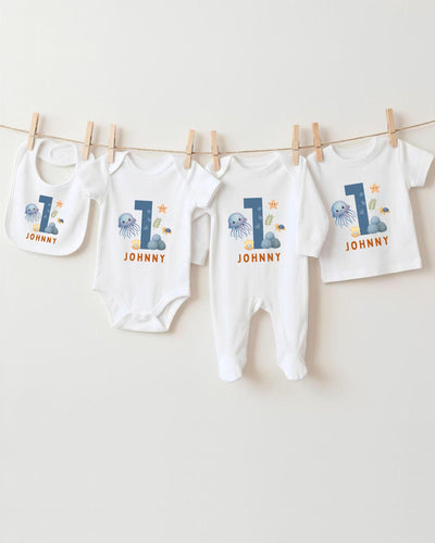 A collection of white baby clothes, including bodysuits and pajamas, with the number 1 printed on them. The clothes are hanging on a clothesline, with the number 1 prominently displayed on each item.