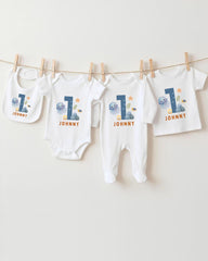 A collection of white baby clothes, including onesies and pajamas, with the number 1 printed on them. The clothes are hanging on a clothesline, with the number 1 prominently displayed on each item.