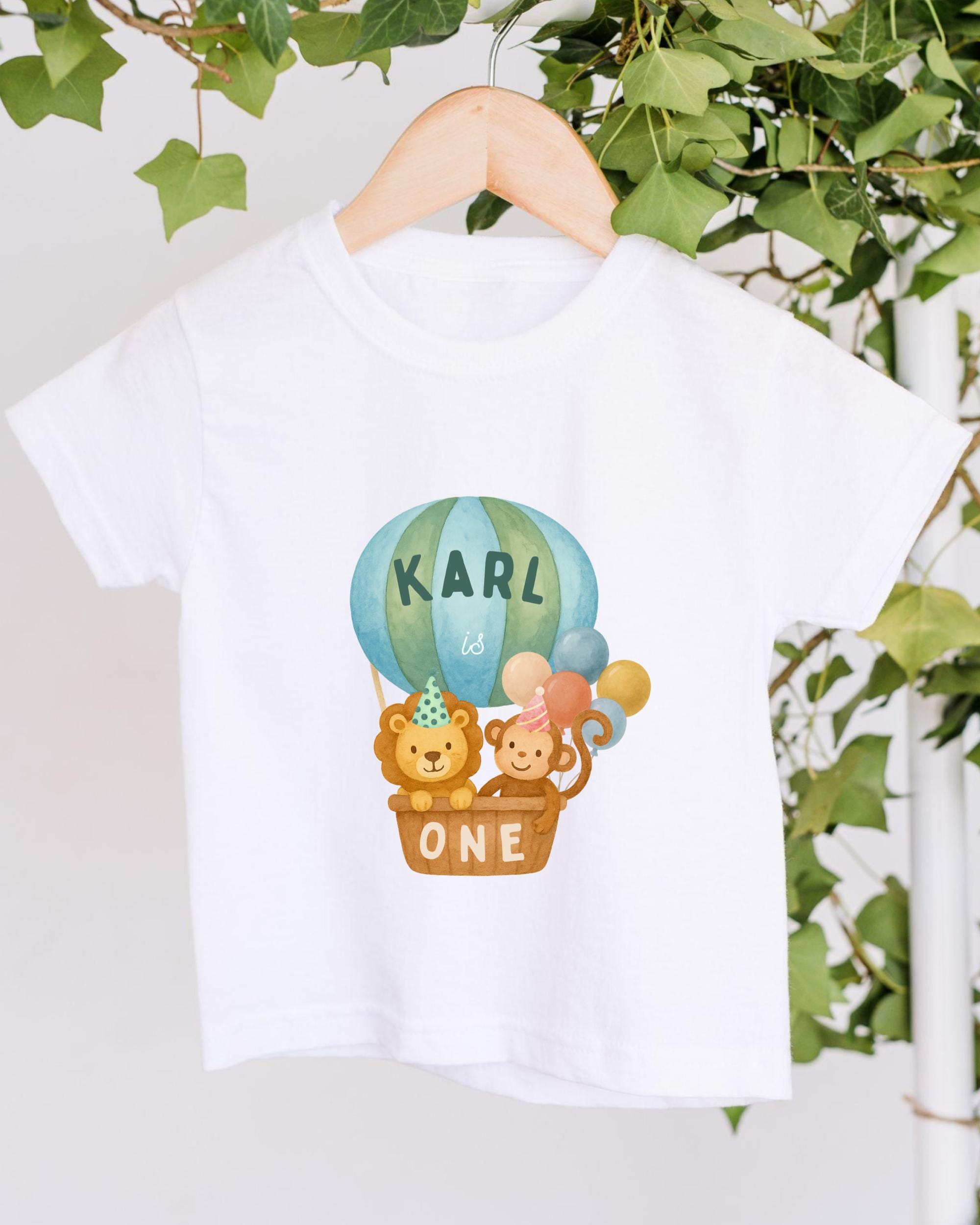 A white t-shirt with a printed design of a hot air balloon carrying a lion and a monkey, along with the text "KARL is ONE".