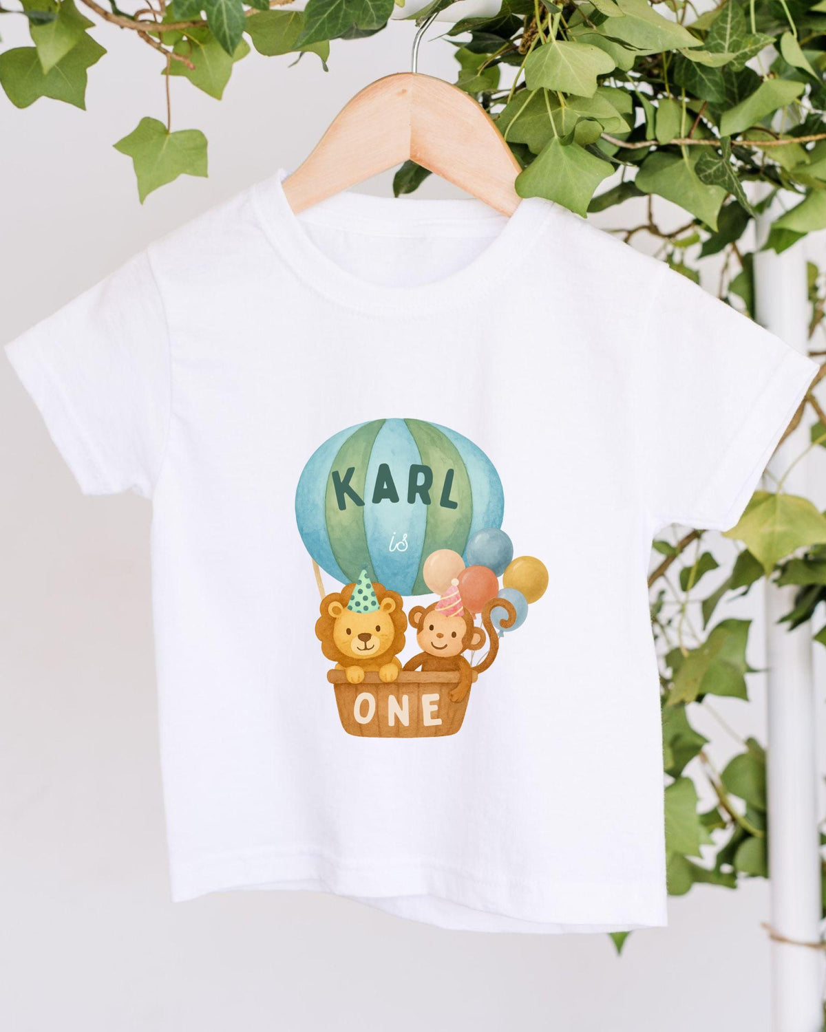 A white t-shirt with a printed design of a hot air balloon carrying a lion and a monkey, along with the text "KARL is ONE".