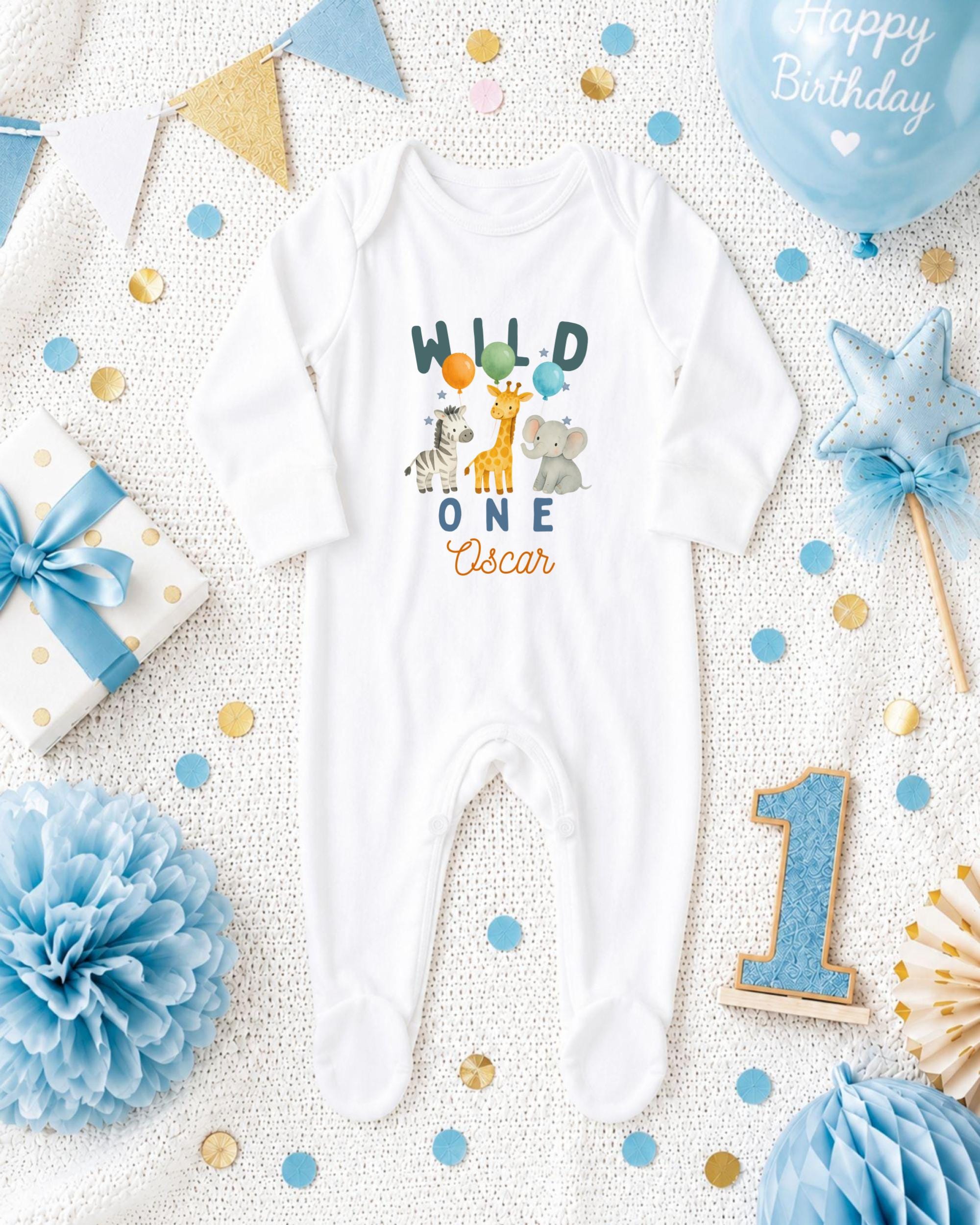 A white onesie with a wild animal print and the text "Wild One Oscar" printed on it, surrounded by various baby-themed items such as a blue and gold gift box, a blue and gold star, and a blue and gold confetti.