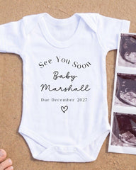 A white onesie with text and a heart symbol, placed next to a photograph of an ultrasound image.