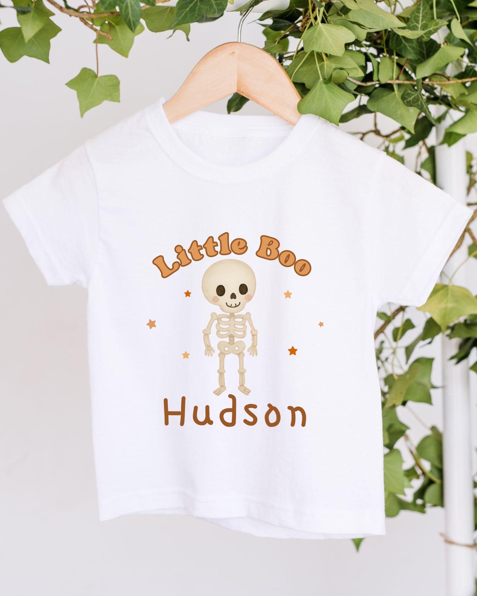 A white t-shirt with a skeleton graphic and the text "Little Boo Hudson" printed on it.