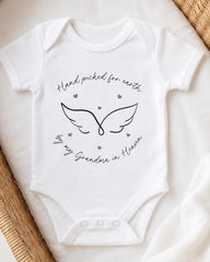A white baby onesie with a graphic design and text on it, placed on a white surface.