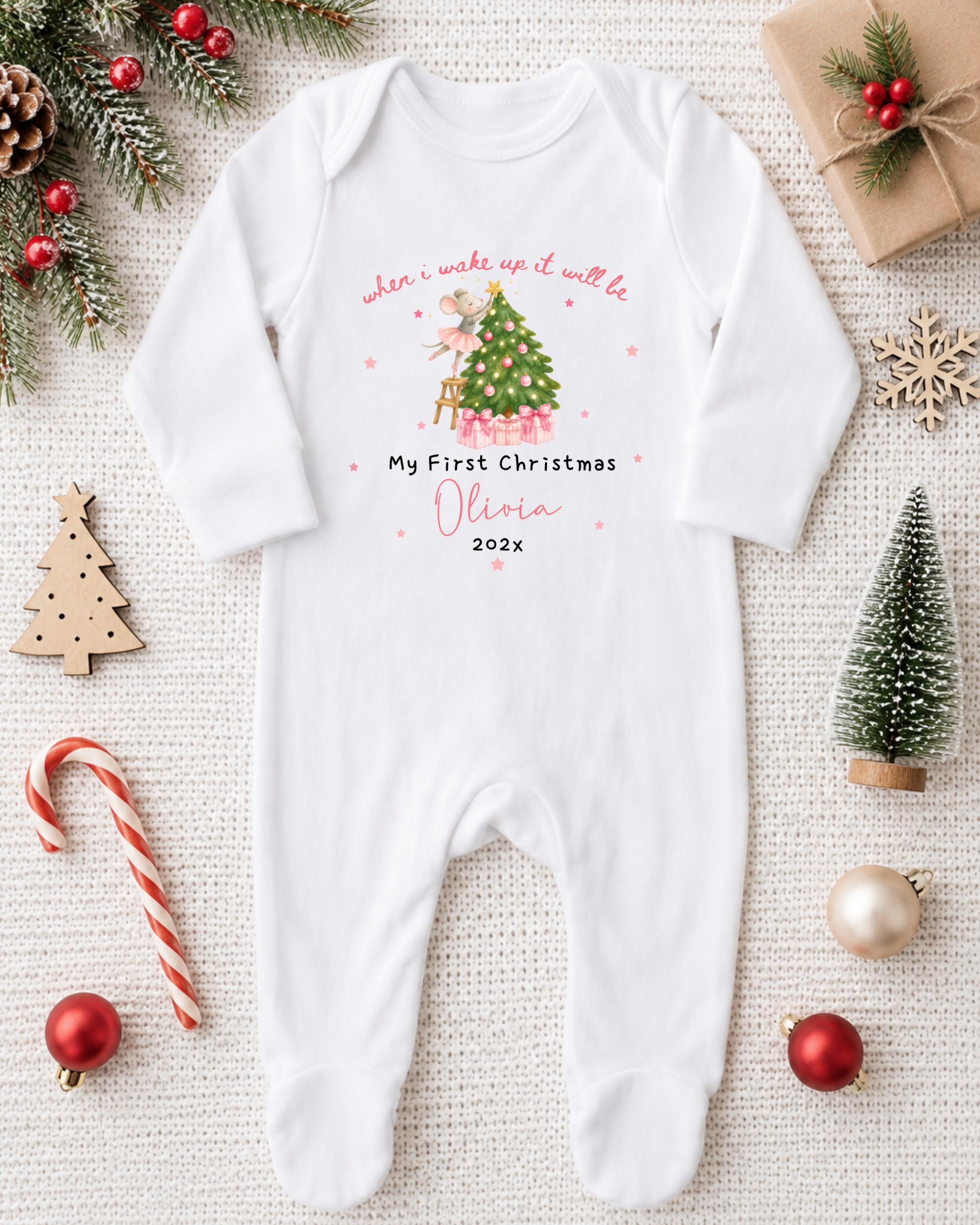 A white onesie with a Christmas tree design and text, surrounded by Christmas decorations and ornaments.