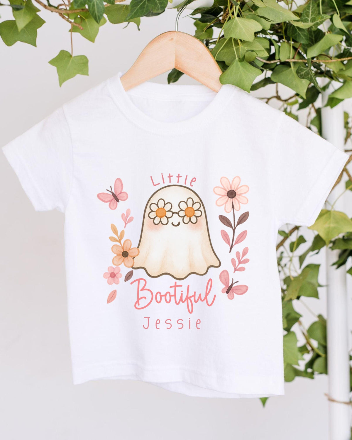 A white t-shirt with a graphic design featuring a ghost surrounded by flowers and butterflies, with the text "Little Bootful Jessie" printed on it.