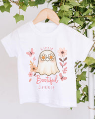 A white t-shirt with a graphic design featuring a ghost surrounded by flowers and butterflies, with the text "Little Bootful Jessie" printed on it.