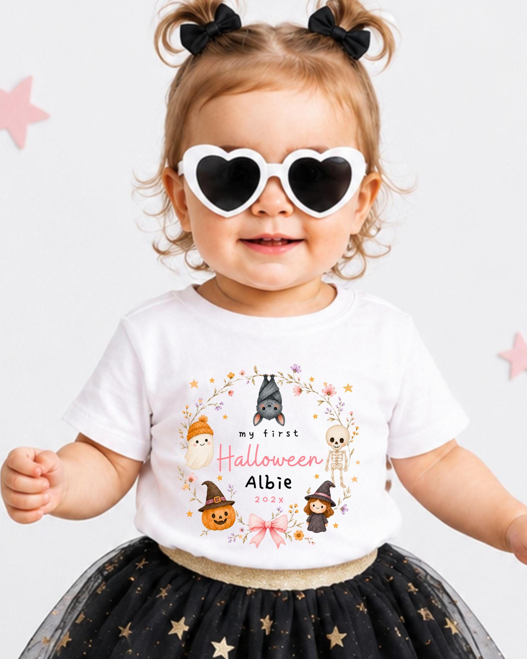 A young girl wearing a white t-shirt with a Halloween-themed design, heart-shaped sunglasses, and a black and gold tutu skirt.