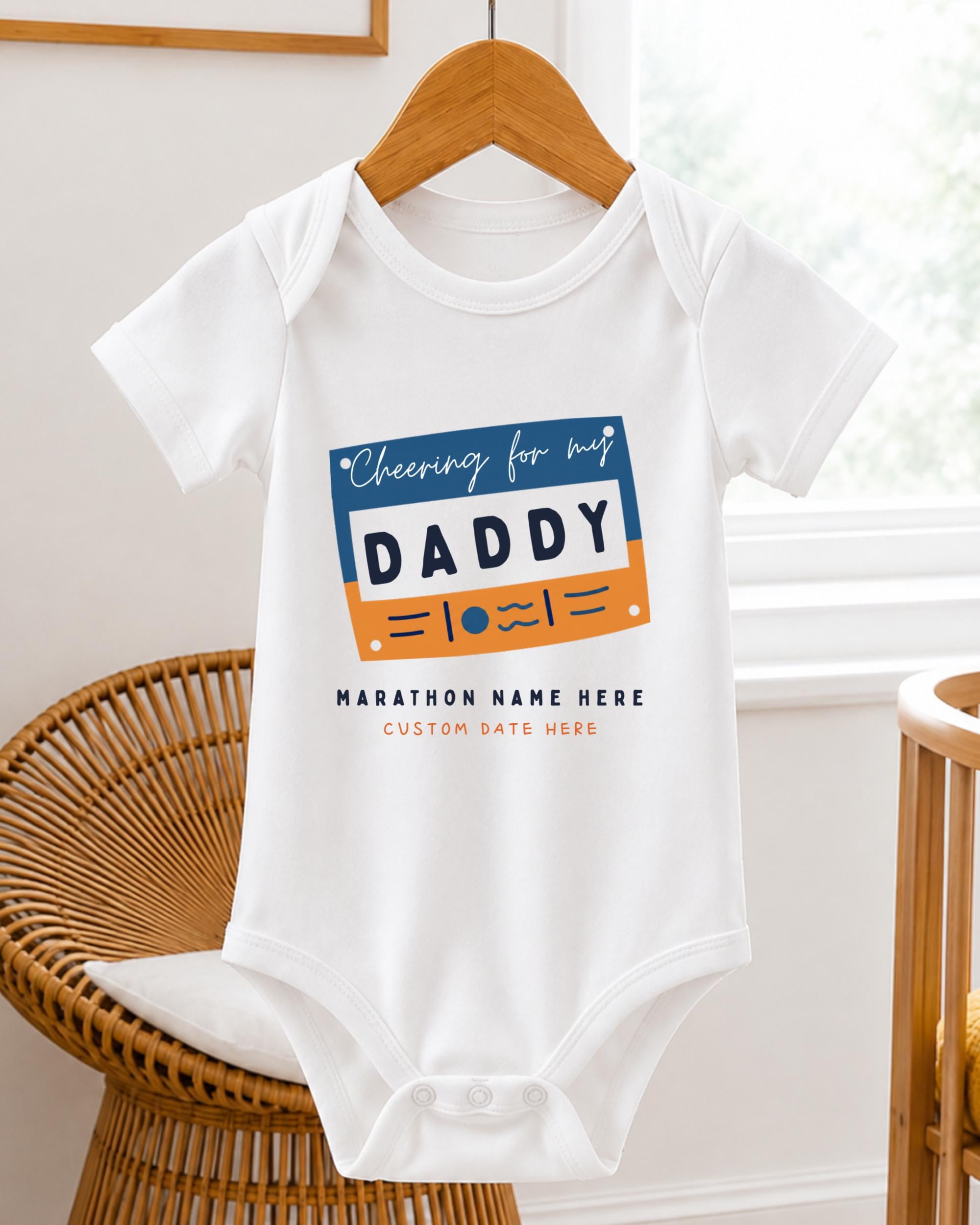 A white baby onesie with a graphic design on it, hanging on a wooden hanger.