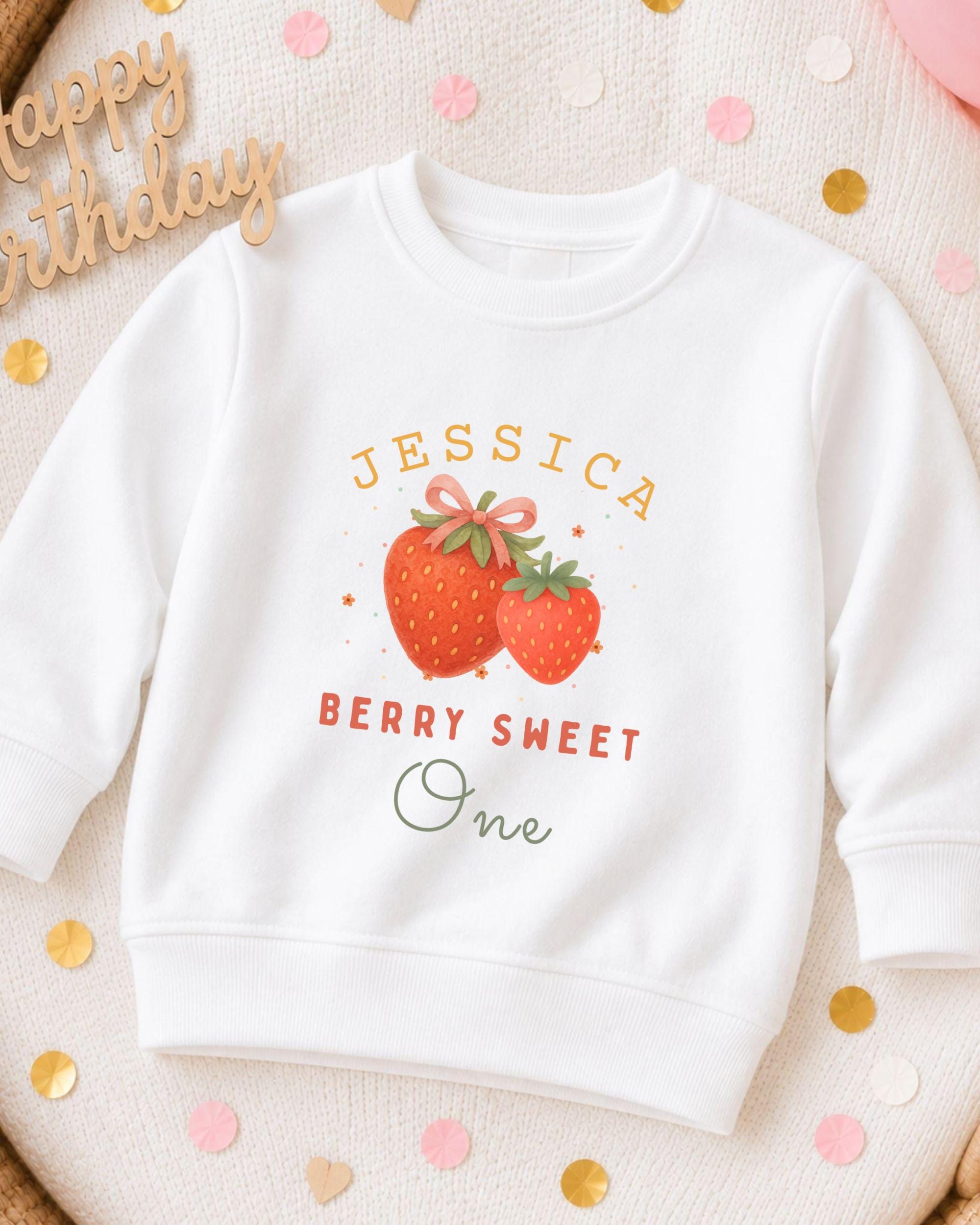 A white sweatshirt with a personalized design featuring a strawberry and the text "JESSICA BERRY SWEET One" printed on it.
