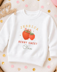 A white sweatshirt with a personalized design featuring a strawberry and the text "JESSICA BERRY SWEET One" printed on it.