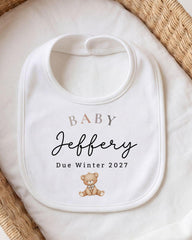 A white baby bib with the name "Jebfery" and the date "Due Winter 2027" printed on it, along with a teddy bear image.