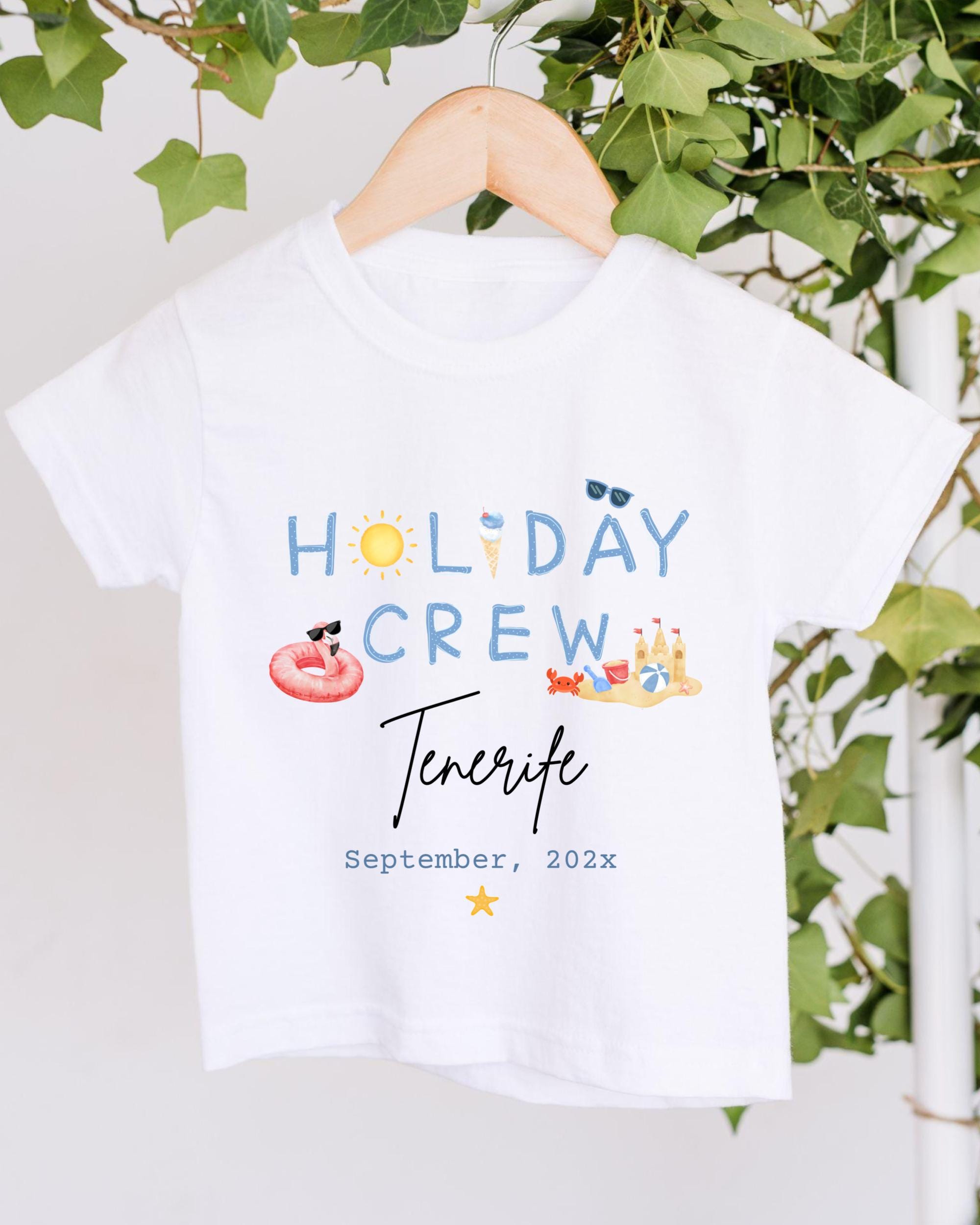 A white t-shirt with the text "HOLIDAY CREW Tenerife" printed on it, along with various summer-themed illustrations such as a sun, sunglasses, a beach ball, and a sandcastle.