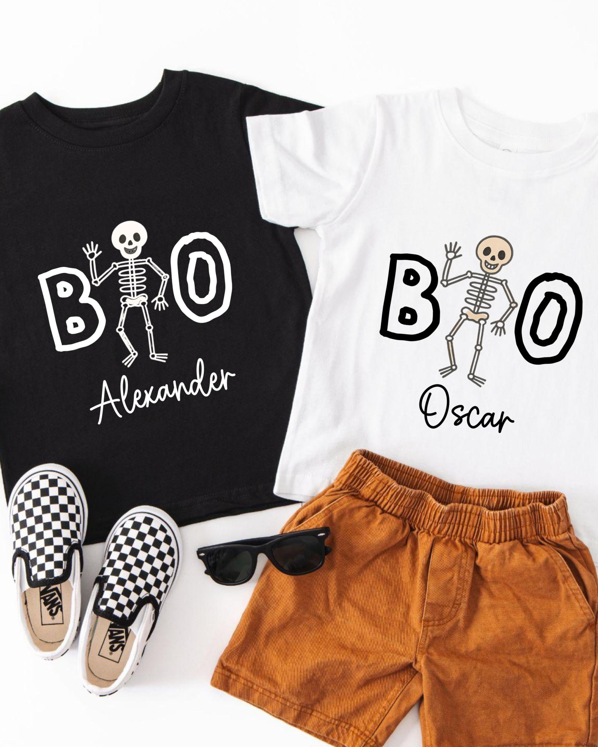 A black t-shirt with a skeleton design and the name "Alexander" printed on it, a white t-shirt with the same skeleton design and the name "Oscar" printed on it, a pair of brown shorts, and a pair of black and white checkered shoes.