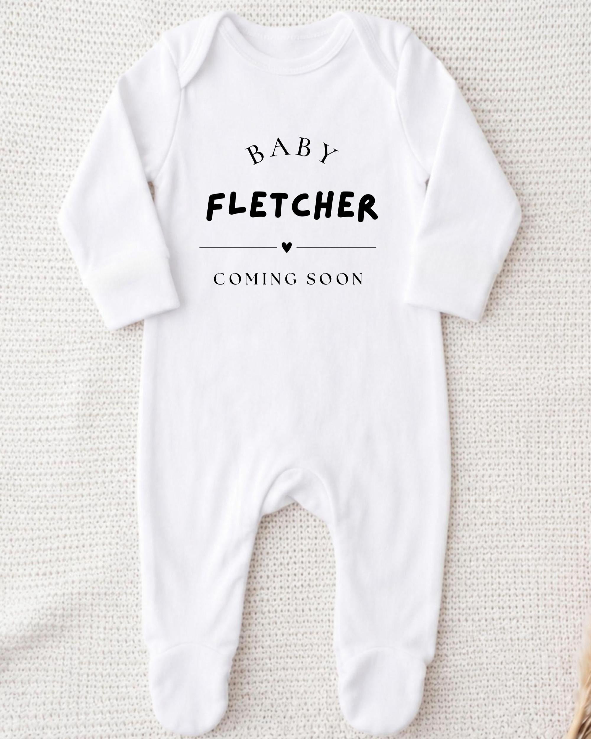 A white onesie with the text "BABY FLETCHER COMING SOON" printed on it.