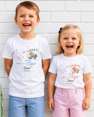 Two children, a boy and a girl, are standing next to each other and smiling. They are wearing matching white t-shirts with a cartoon character and text printed on them.