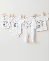 A row of four white baby clothes, including onesies and bibs, hanging on a clothesline.