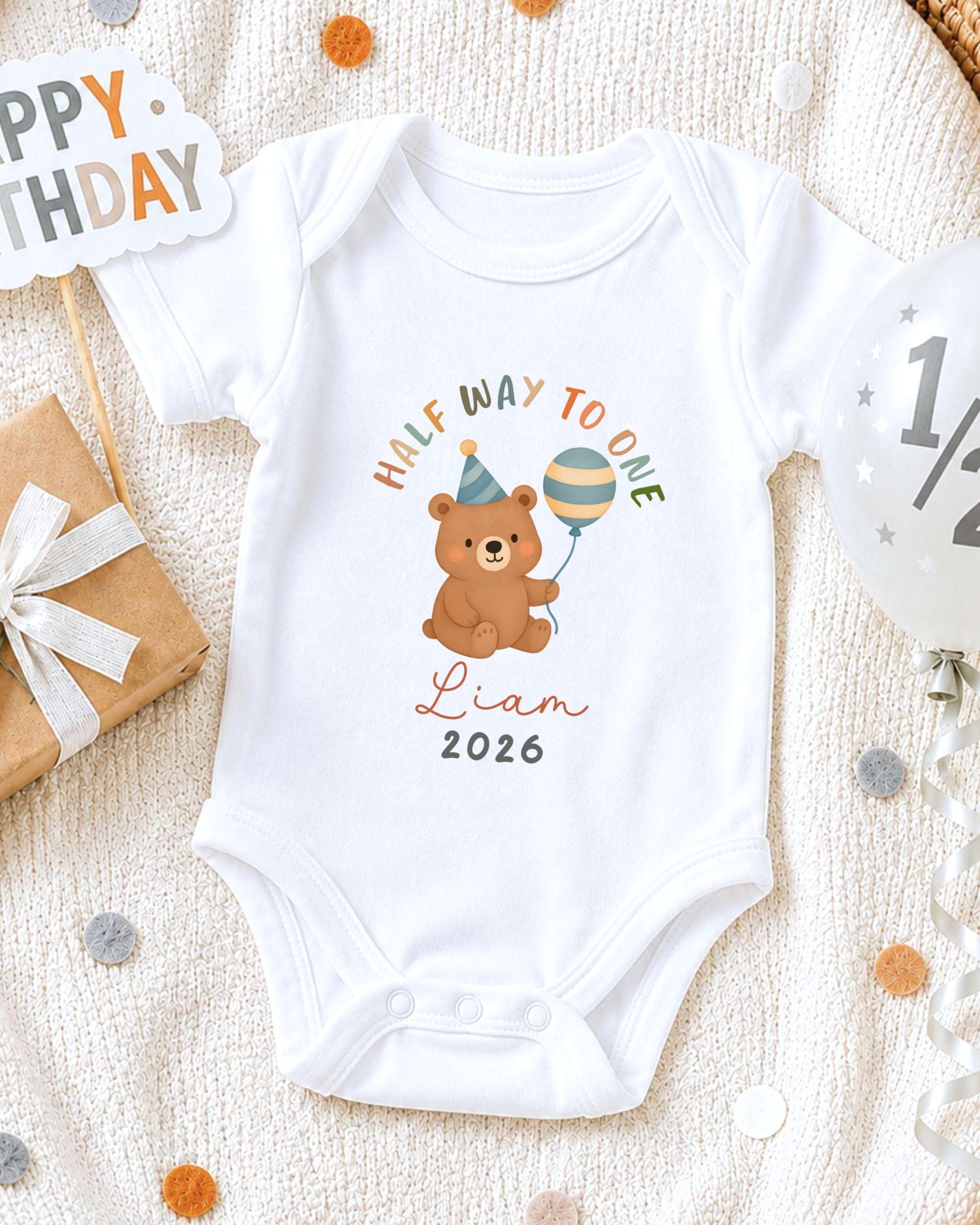 A white onesie with a cartoon bear and a balloon, along with a "Happy Birthday" sign and confetti, suggesting a celebration of a child's first birthday.