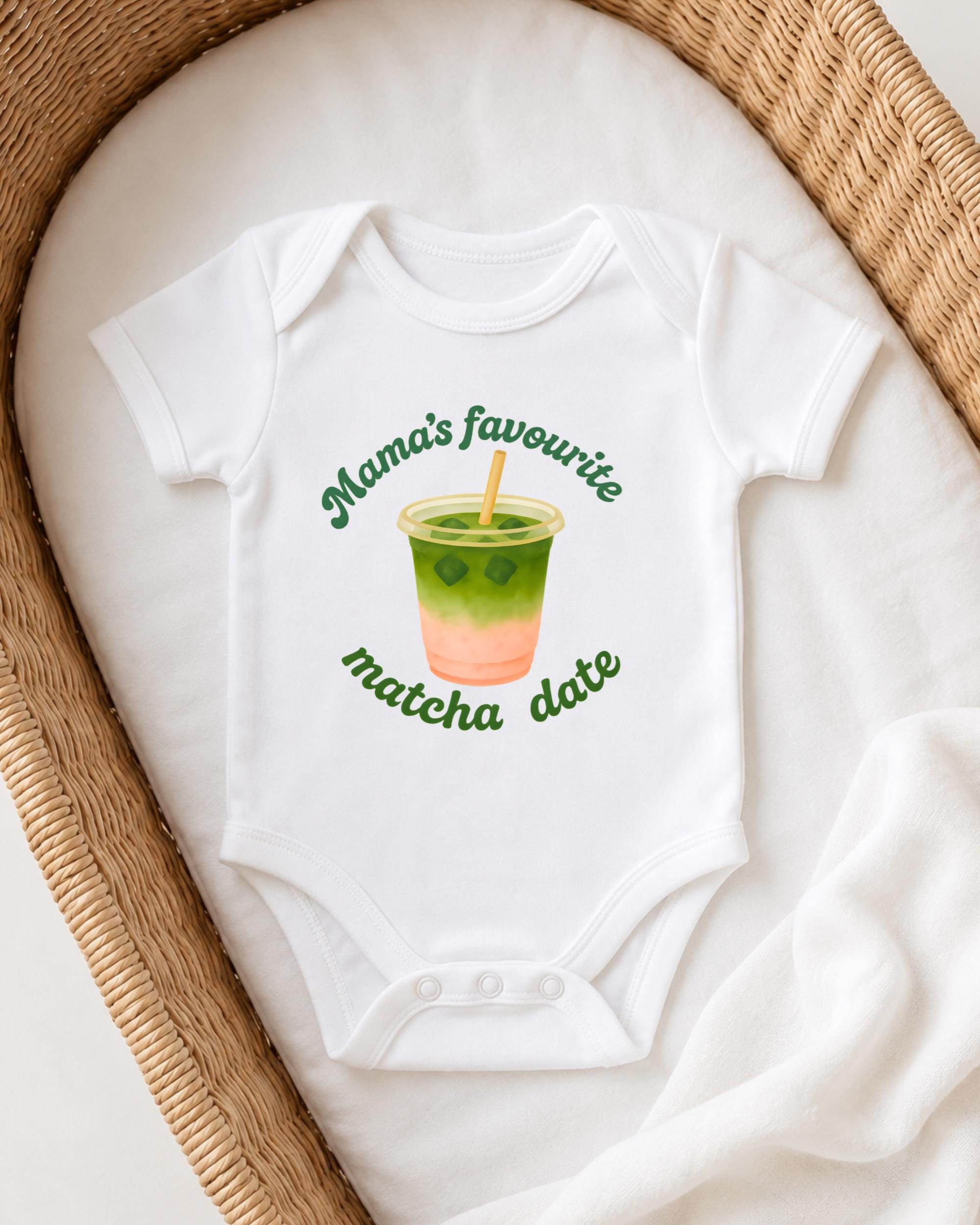 A white onesie with a graphic of a green drink and the text "Mama's favourite matcha date" printed on it, placed on a white blanket.