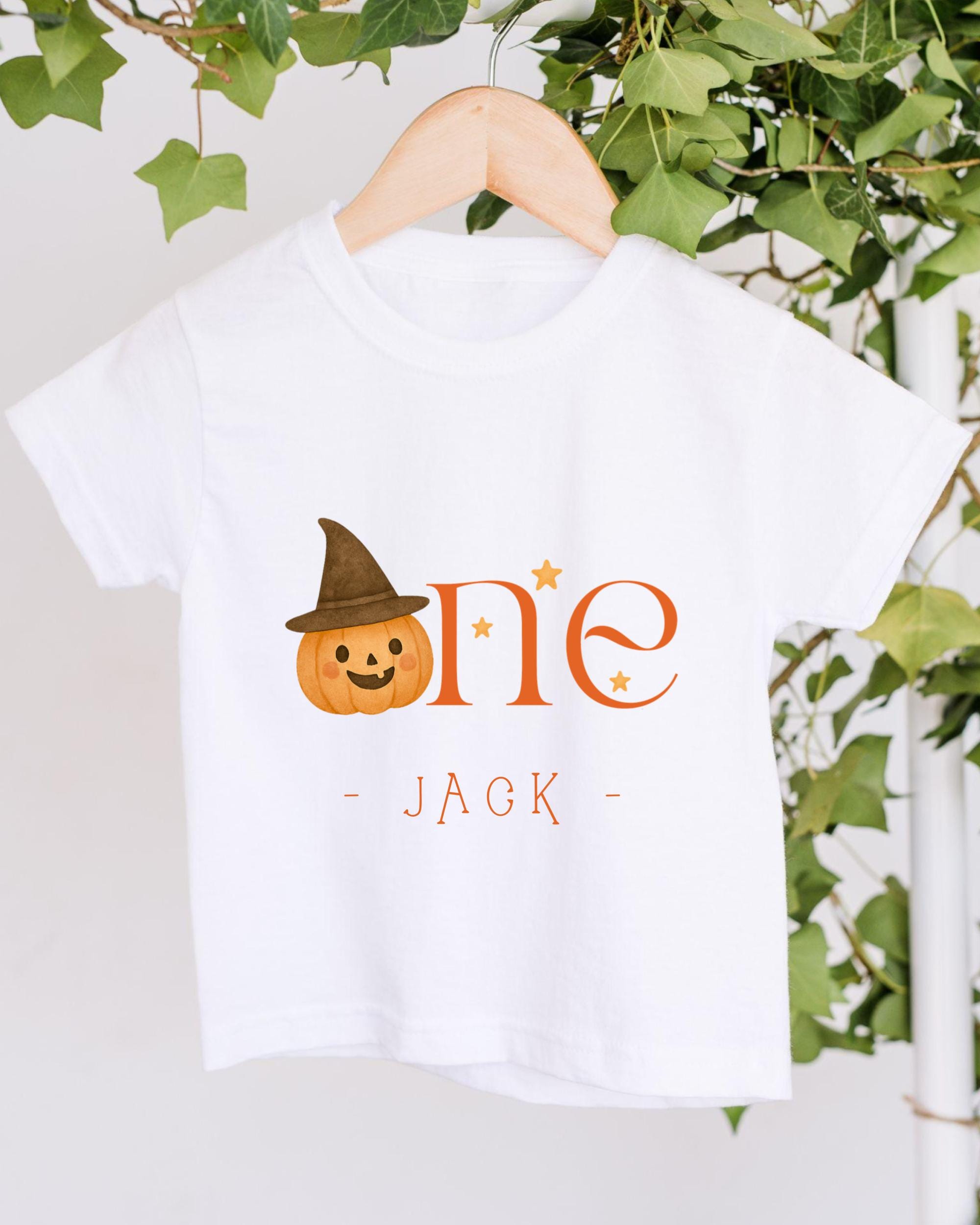 A white t-shirt with a pumpkin graphic and the text "One Jack" printed on it, hanging on a wooden hanger.