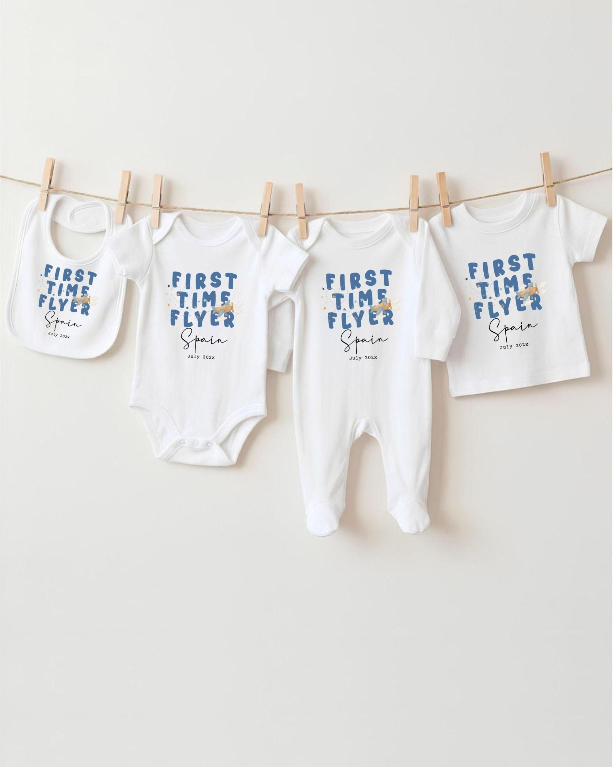 A row of white baby clothes with blue text printed on them, hanging on a clothesline.
