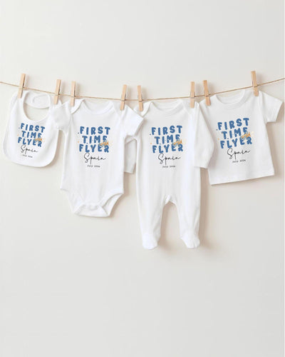 A row of white baby clothes with blue text printed on them, hanging on a clothesline.