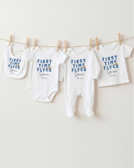 A row of white baby clothes with blue text printed on them, hanging on a clothesline.