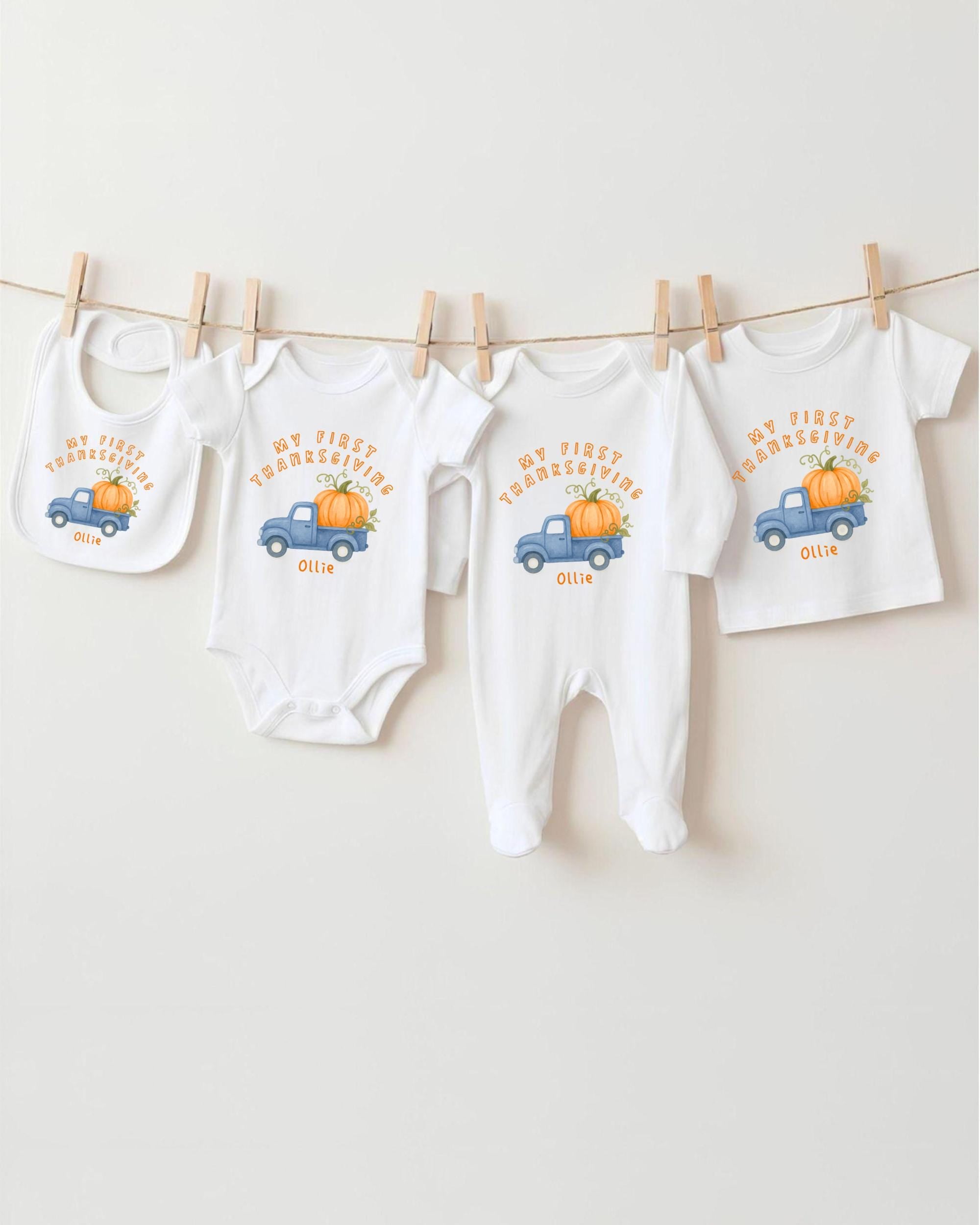 A collection of white baby clothes, including onesies and bibs, with a pumpkin and truck design, hanging on a clothesline.