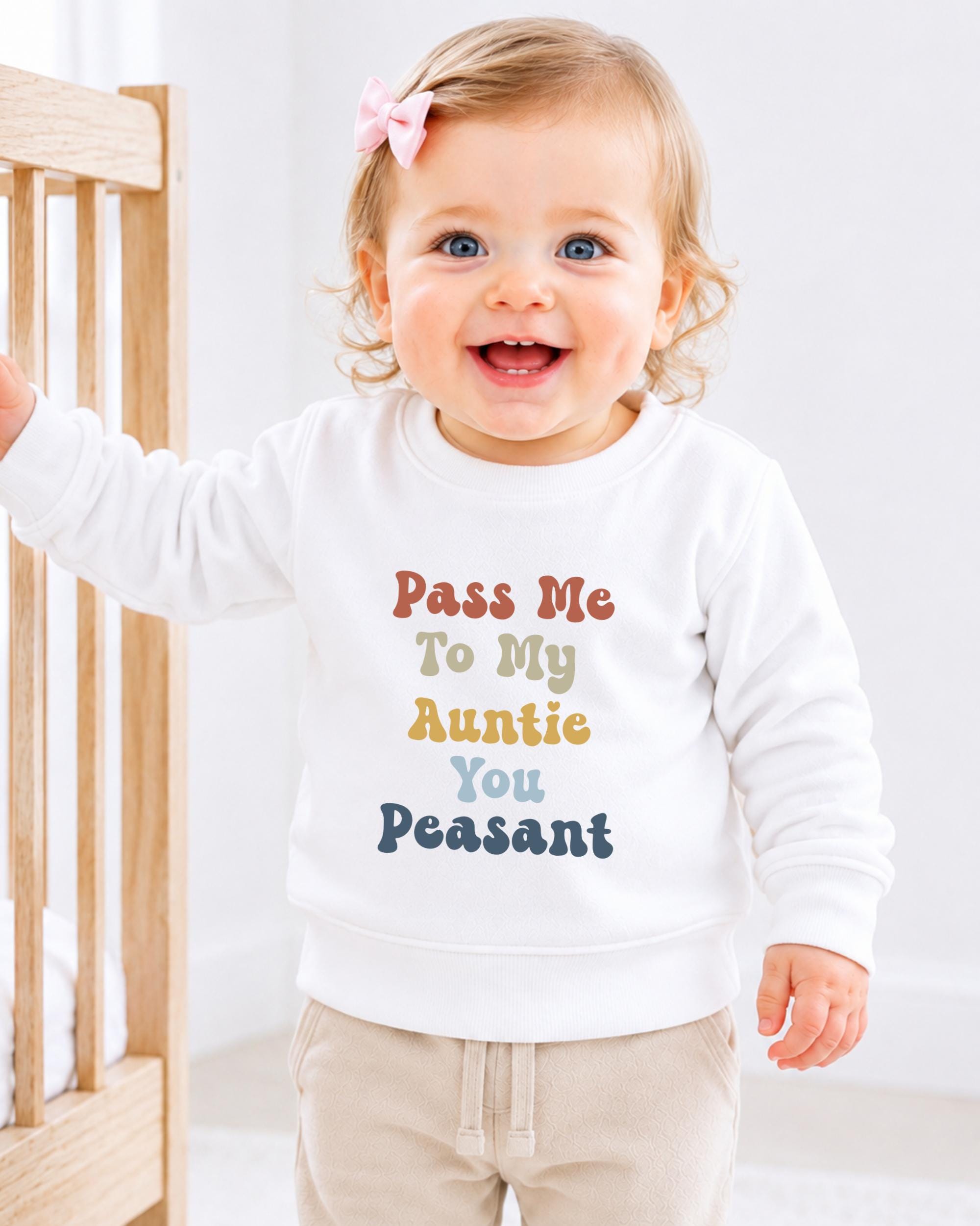 A smiling baby girl wearing a white sweater with text on it.