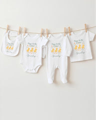 A row of baby clothes, including onesies and bibs, hanging on a clothesline.