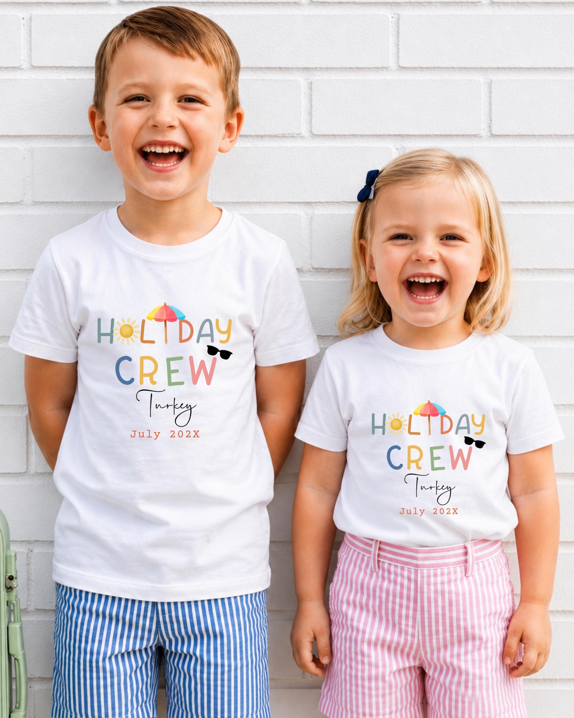 Two children, a boy and a girl, are standing next to each other and smiling, wearing matching white t-shirts with text and graphics.