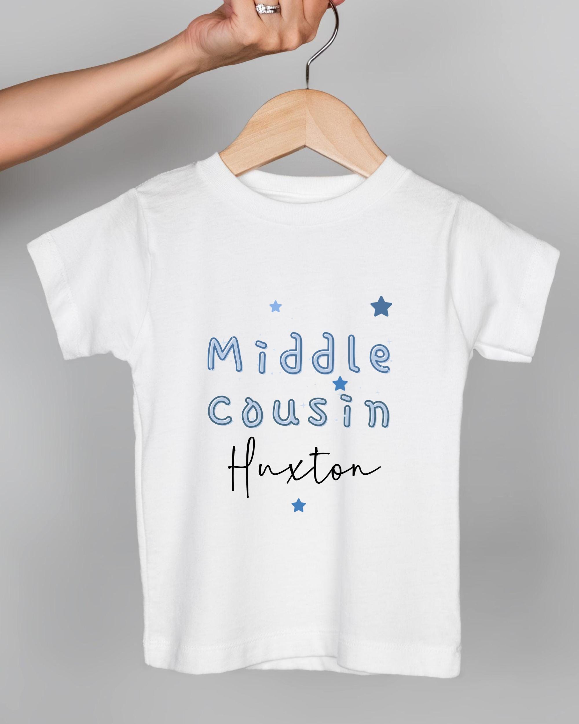 A white t-shirt with blue text and stars printed on it, being held by a person's hand.