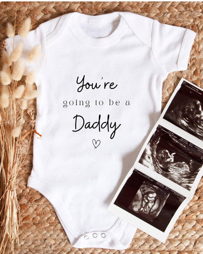 White Baby Vest with black 'You're going to be a Daddy' script and serif lettering and a small outlined heart.