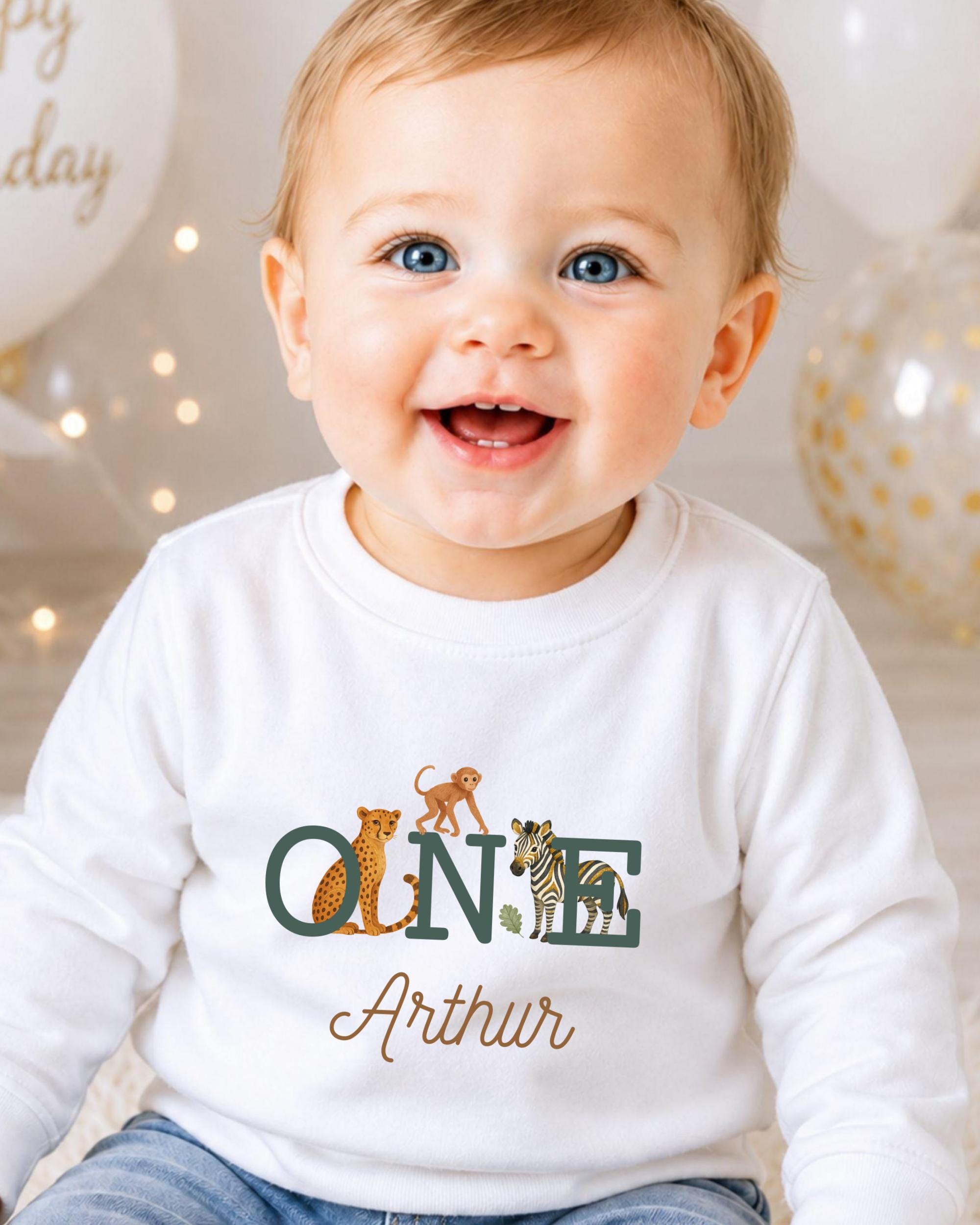 A smiling baby boy wearing a white shirt with a personalized name and animal print.