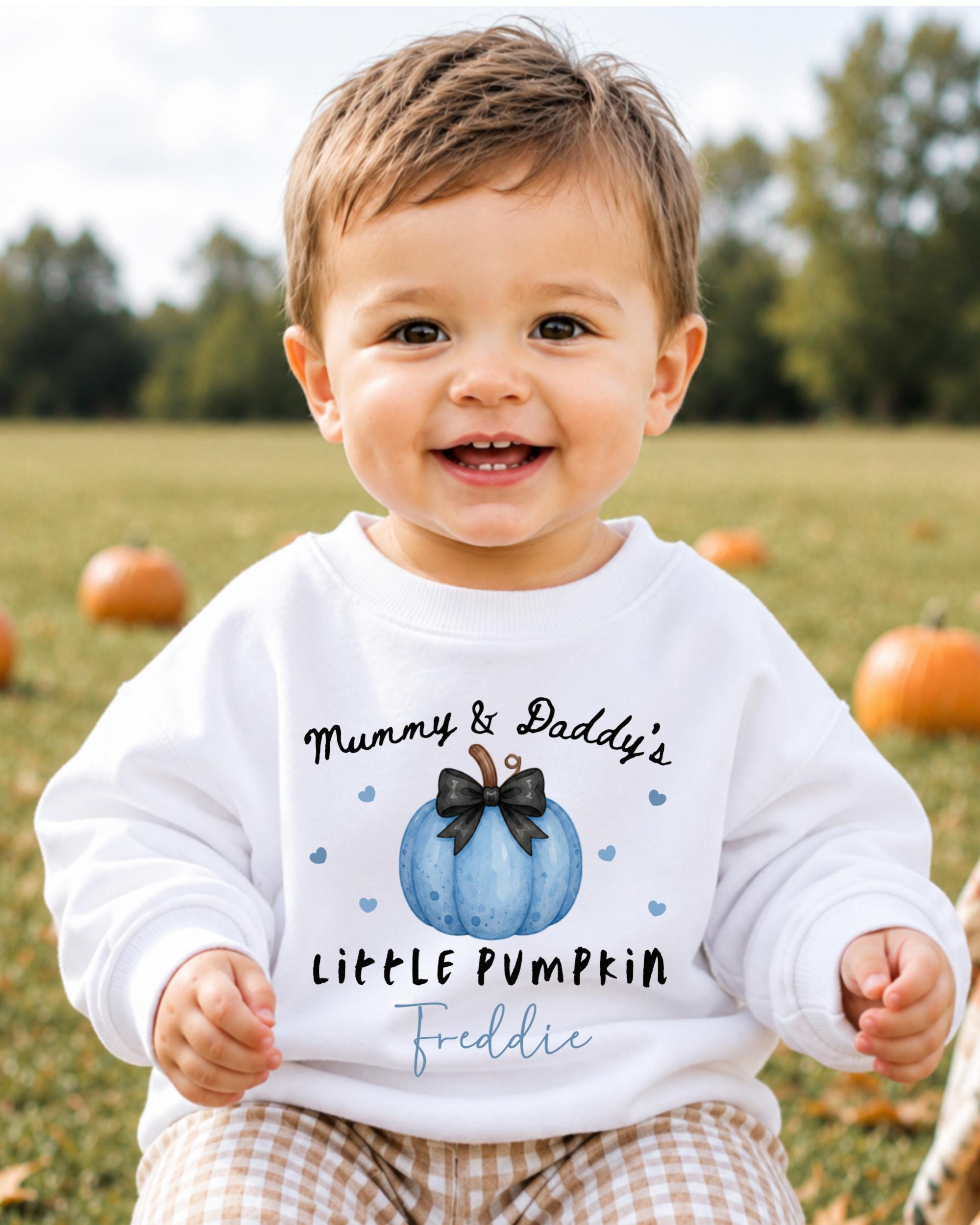 A smiling baby boy wearing a white sweatshirt with a pumpkin design and text that says "Mummy & Daddy's LITTLE PUMPKIN Freddie".