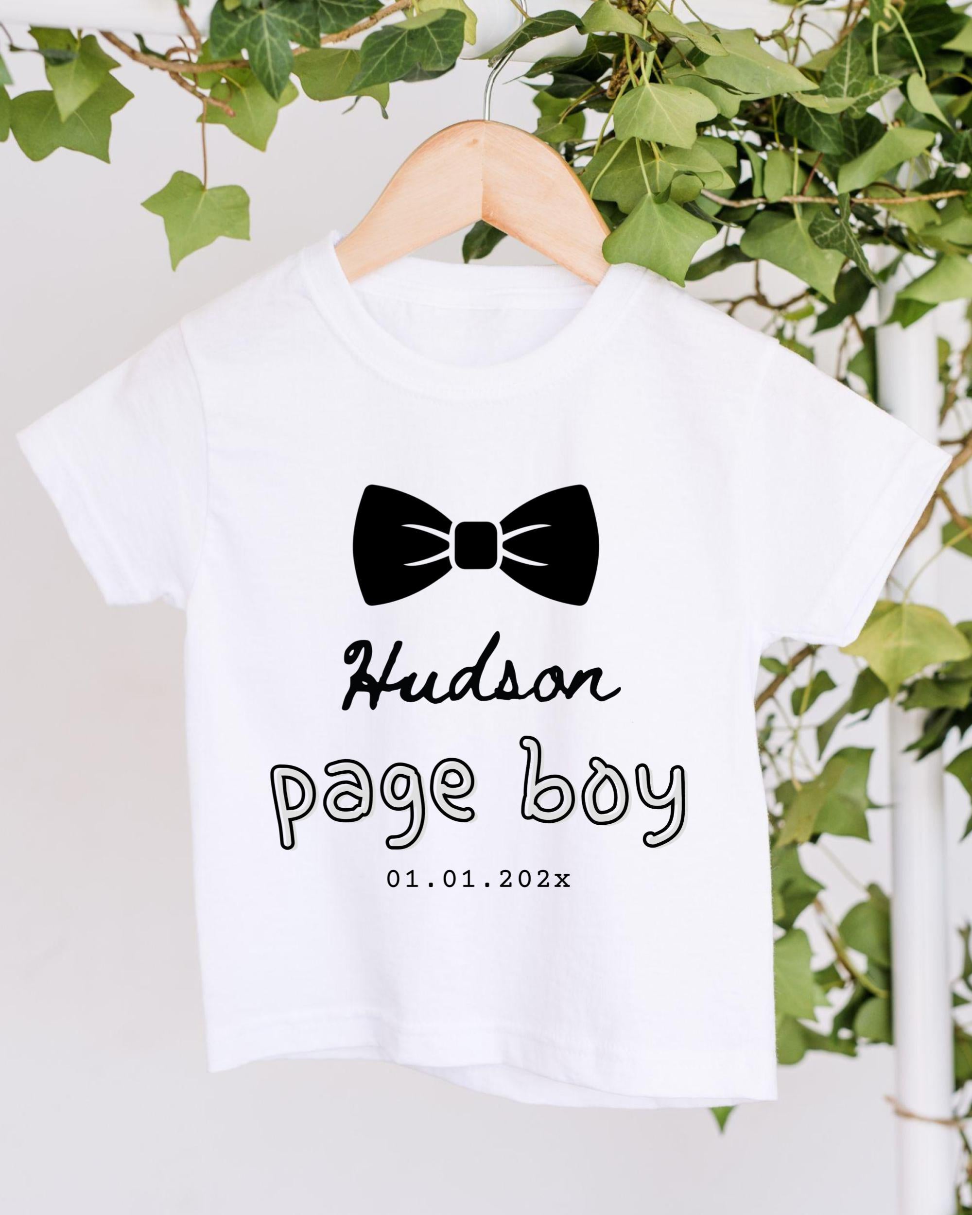 A white t-shirt with a black bow tie and text printed on it, hanging on a wooden hanger.