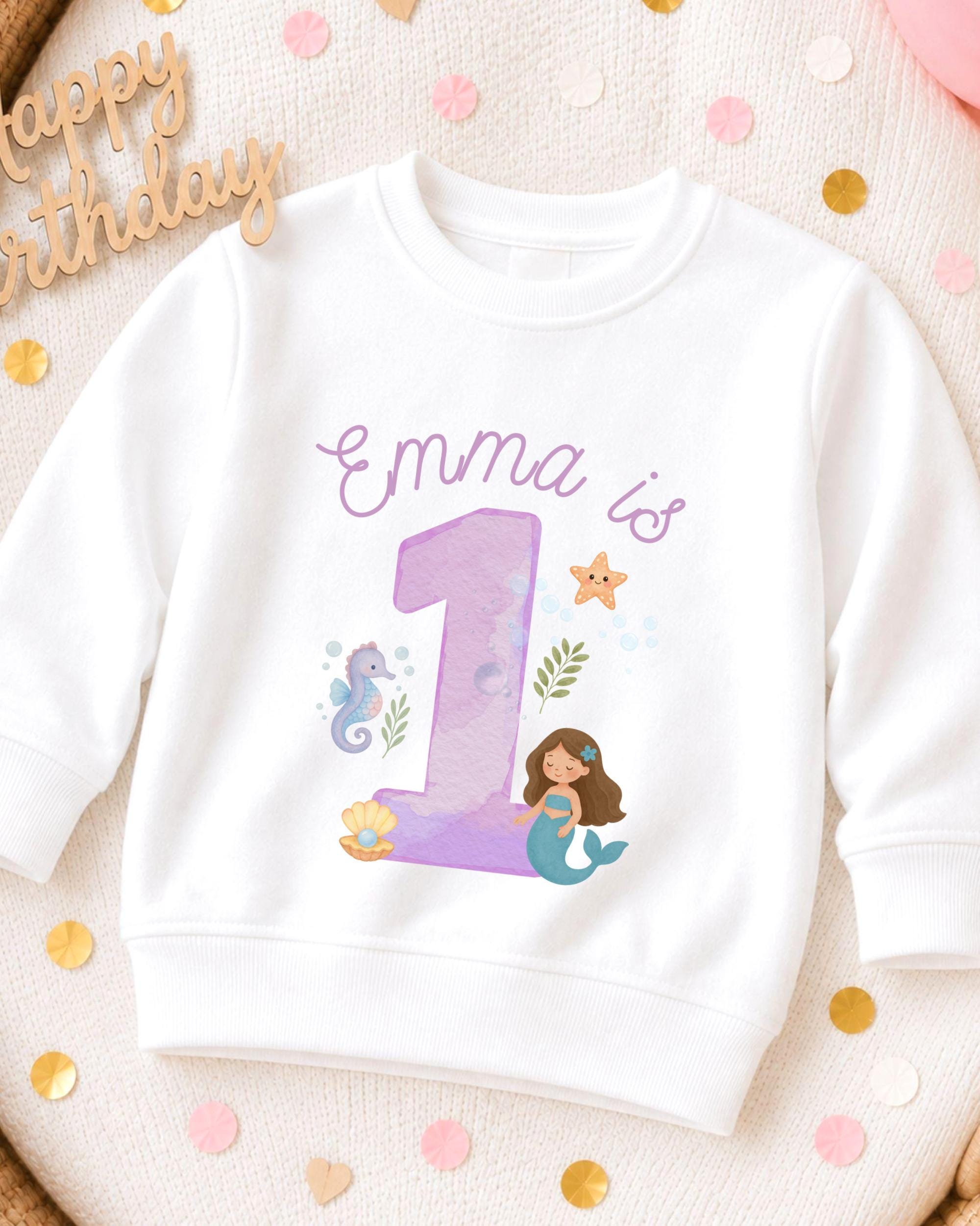 A white sweatshirt with a mermaid and a number 1 printed on it, surrounded by confetti.