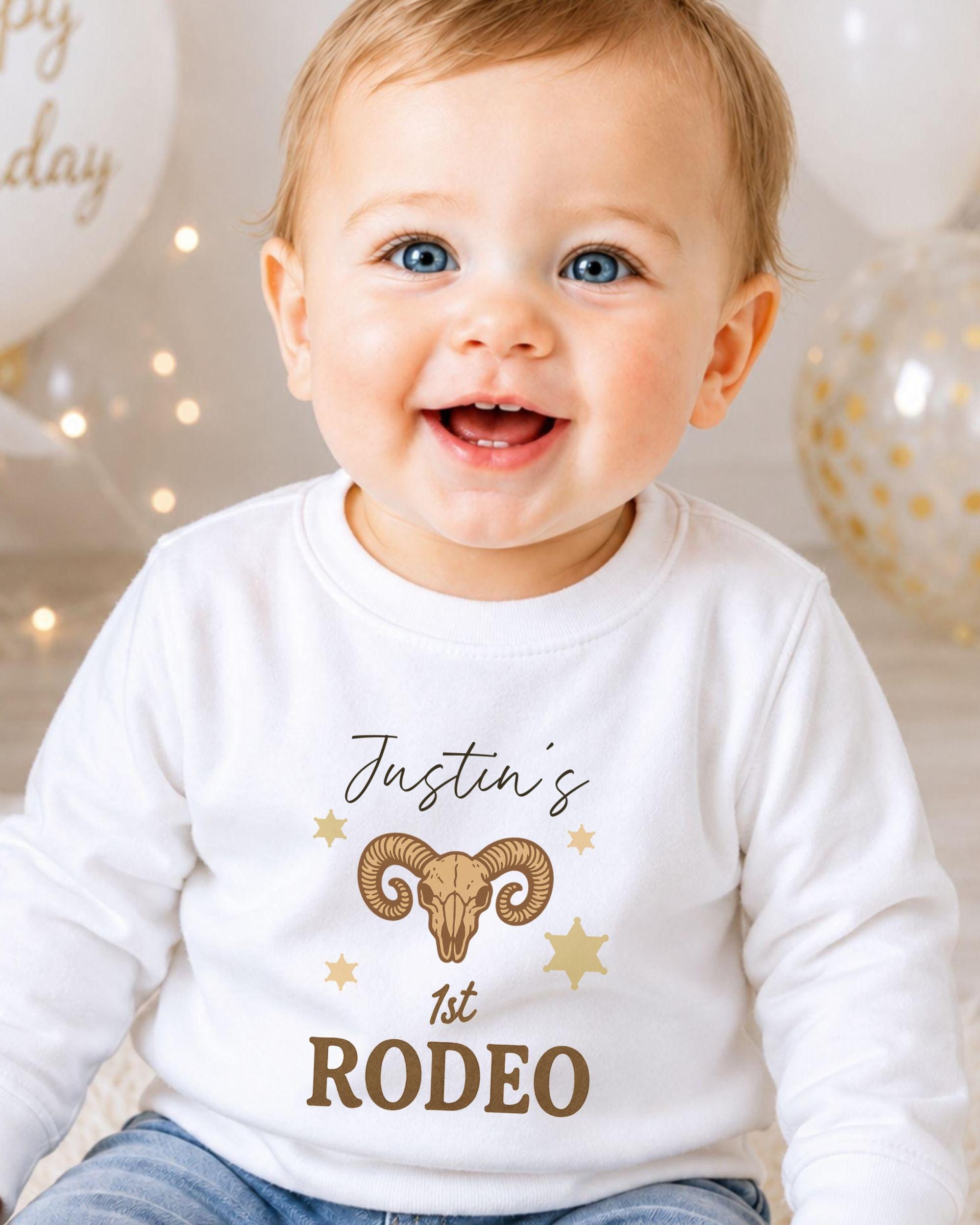A smiling baby boy wearing a white shirt with a graphic design and text.