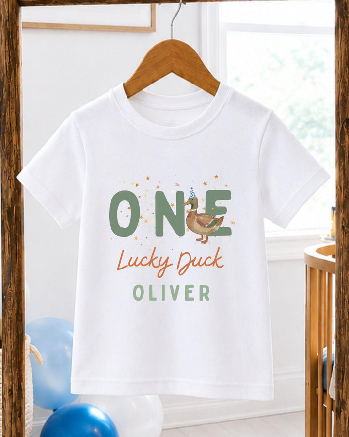 A white t-shirt with a graphic design featuring a cartoon duck and the text "One Lucky Duck Oliver" printed on it.