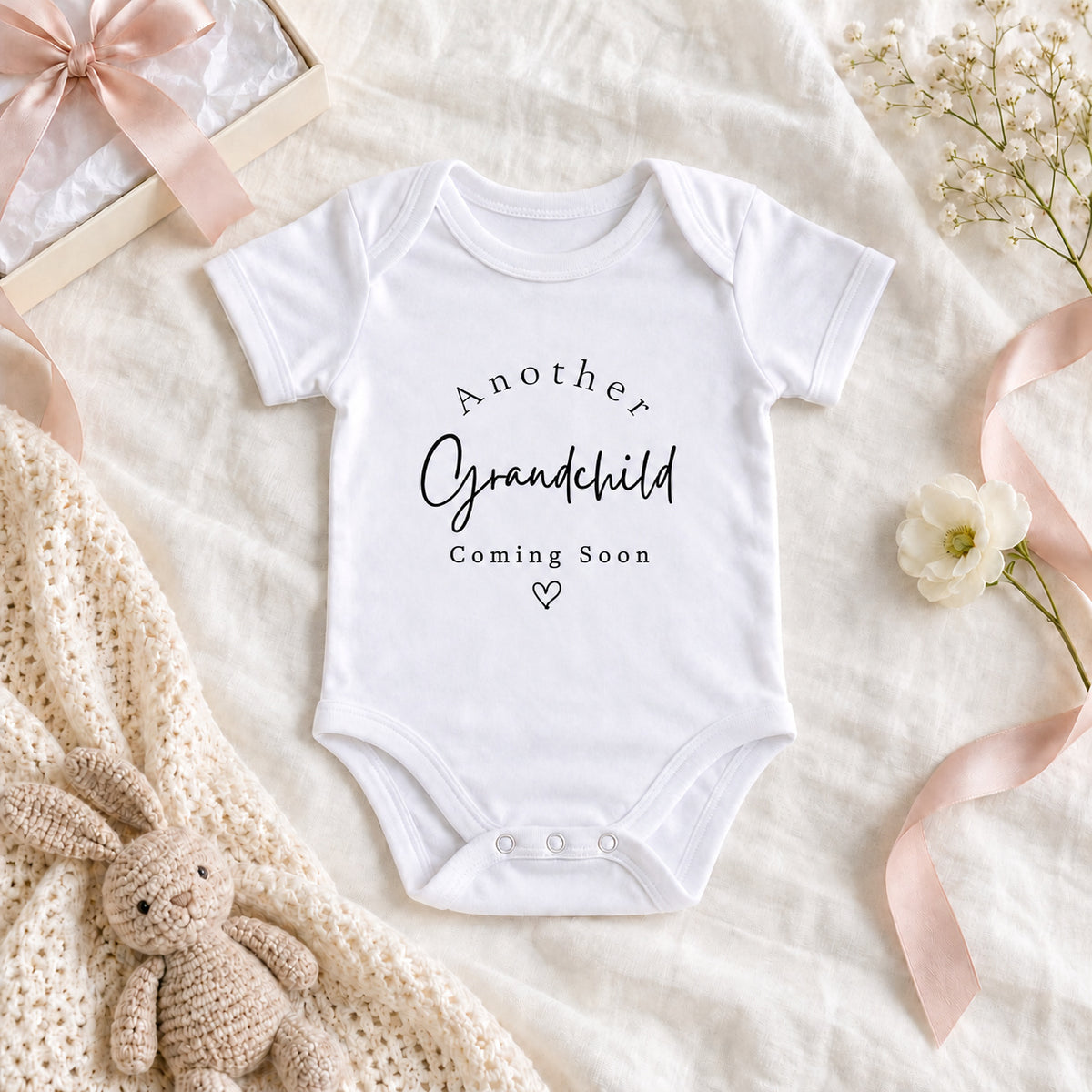 Another grandchild pregnancy announcement Baby Vest on a beige flat lay with gift box, cream ribbon, wooden milestone block and eucalyptus