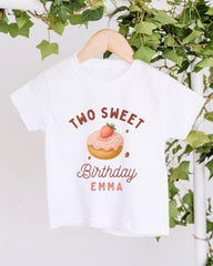 A white t-shirt with a graphic design featuring a strawberry donut and the text "Two Sweet Birthday Emma" printed on it.