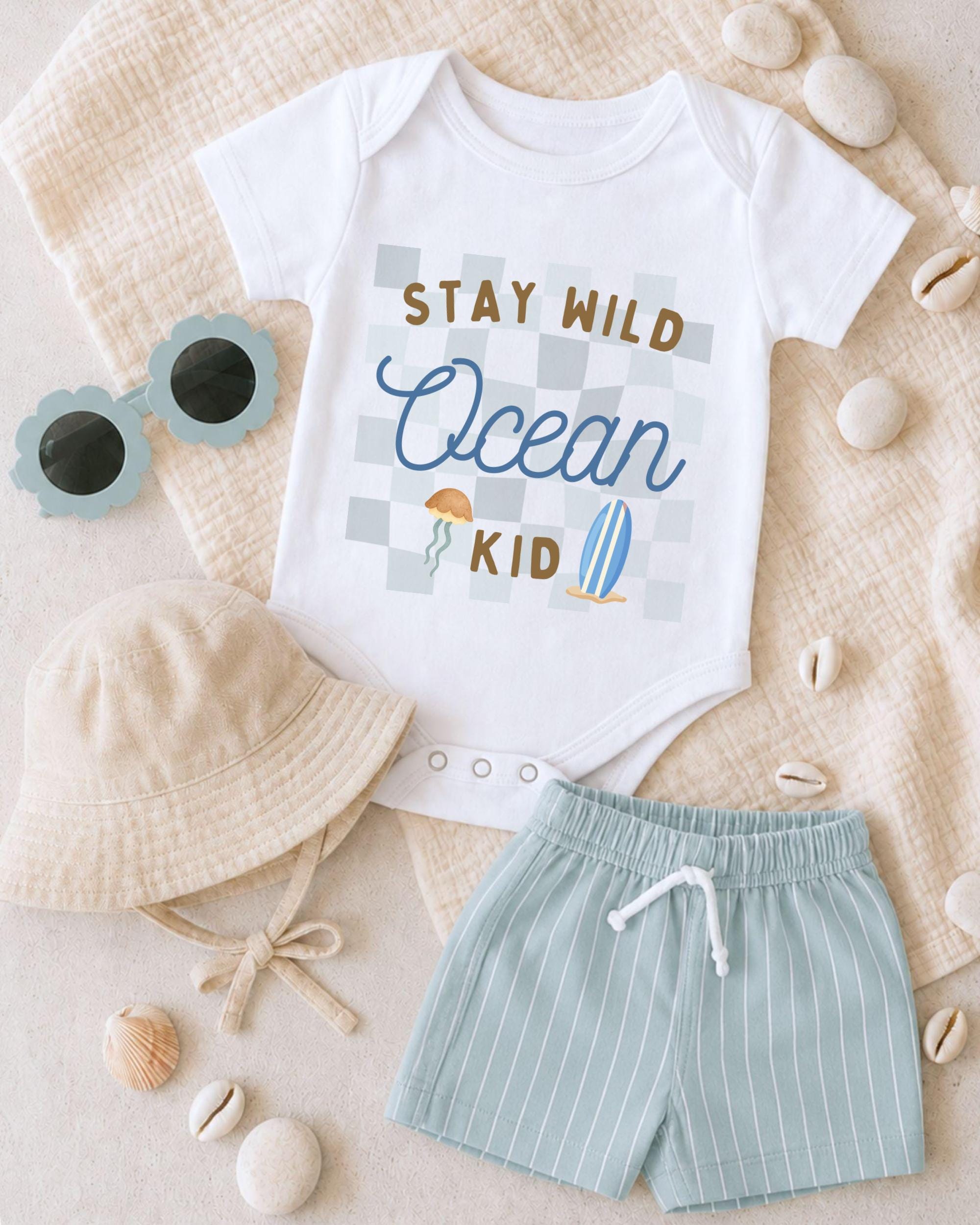 A baby's outfit consisting of a white onesie with a checkered pattern, a beige bucket hat, and striped shorts, along with a pair of sunglasses and some seashells, all laid out on a beige surface.