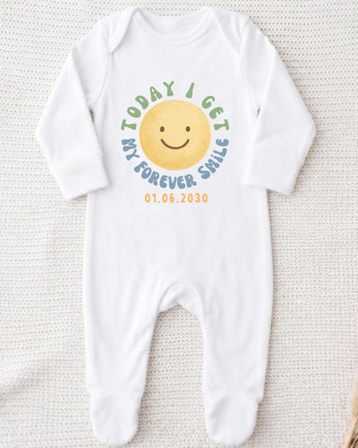 A white bodysuit with a smiley face design and text printed on it.