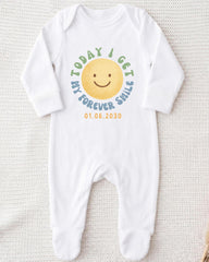 A white onesie with a smiley face design and text printed on it.