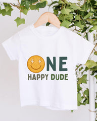 A white t-shirt with a smiley face and the text "ONE HAPPY Dude" printed on it, hanging on a wooden hanger.