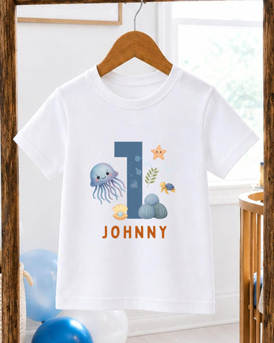 A white t-shirt with a graphic design featuring a blue jellyfish, a starfish, and other sea creatures, along with the text "JOHNNY" printed on it.