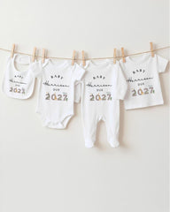 A row of white baby clothes hanging on a clothesline, each with a unique design or text printed on it.