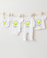 A row of white baby clothes with tennis ball designs hanging on a clothesline.